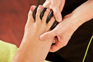 a therapist places hot rocks between a woman's toes as part of her reflexology treatment
